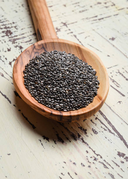 Nutritious chia seeds in wooden spoon for diet food ingredients. Composition of chia seed in wooden spoon on old light wooden background. Nutritious chia seeds in wooden spoon for diet food ingredients. Composition of chia seed in wooden spoon on old light wooden background. vertical. salvia hispanica plant stock pictures, royalty-free photos & images