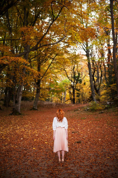 Young beautiful woman standing in a autumn scenario, looking trees.