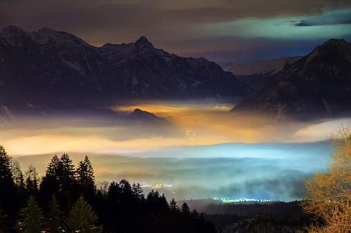 Beautiful winter night view of the city Brand in the valley of the Brandnertal in the mountains of the Alps in Vorarlberg, Austria, with illuminated fog clouds