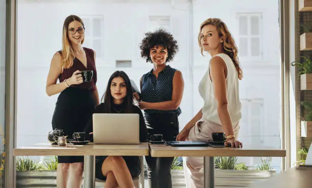 Portrait of four successful young businesswomen together in office. Group of multi-ethnic businesswomen looking at camera.
