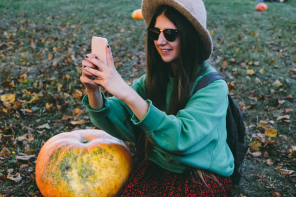 istock Beautiful woman in hat making selfie with pumpkin 1055116136