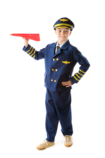 Portrait of a 9 years old young boy with career aspiration of being an airline pilot on white background. He is wearing a pilot suit costume, holding a paper airplane, looking at camera