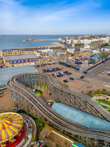 Margate, UK. 13 October 2018. A view over the rides of Dreamland fair and Margate town and seafront on a sunny day. People walking around the rides and in the town.