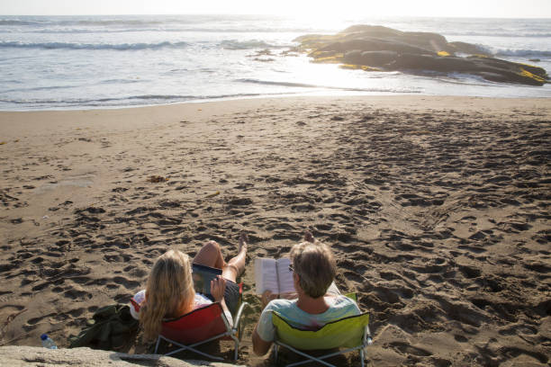 istock Couple sit in chairs on beach at sunset with tablet and book 1055157836
