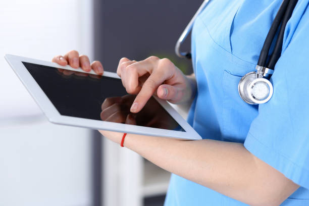 istock Woman doctor using tablet computer while standing straight in hospital office, closeup. Healthcare, insurance and medicine concept. 1055162188