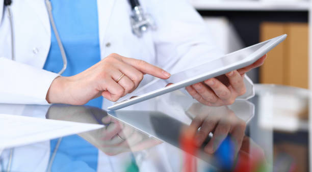 istock Woman doctor using tablet computer while standing straight in hospital office, closeup. Healthcare, insurance and medicine concept. 1055162314