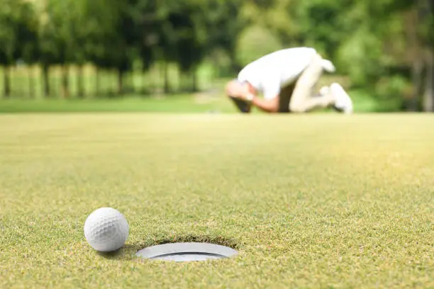 Man golfer feeling disappointed after a putted golf ball missed the hole
