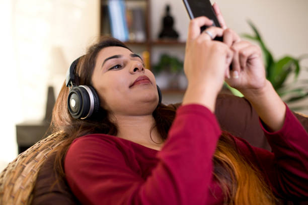 istock Woman using mobile phone and headphones at home 1055191576