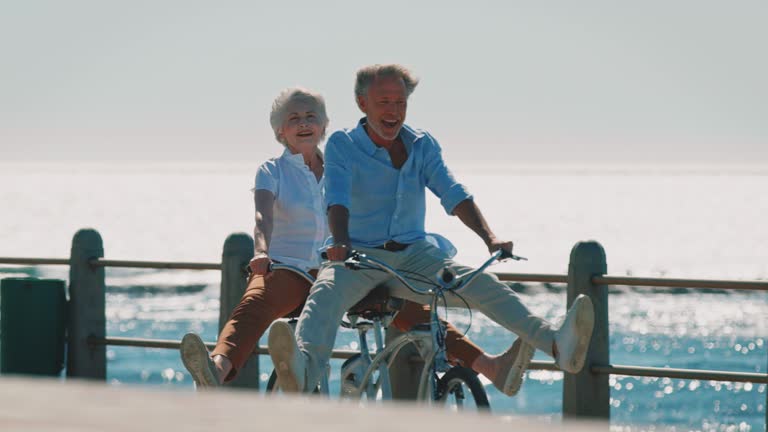 Senior couple riding tandem bike on promenade