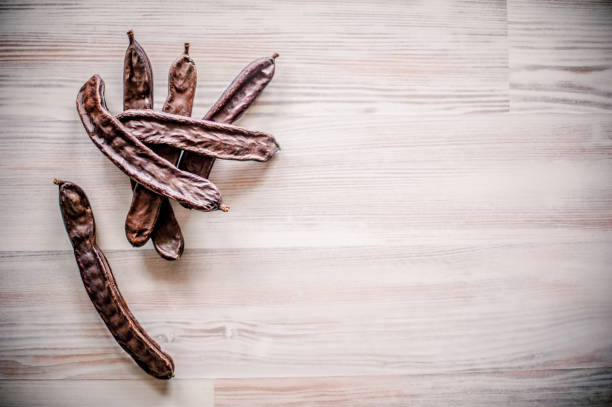 Ripe Carob Pods (Ceratonia siliqua) on Wooden Surface