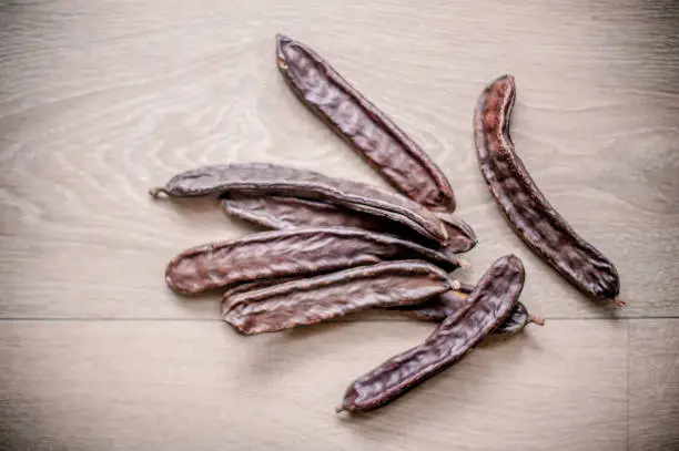 Photo of Ripe Carob Pods (Ceratonia siliqua) on Wooden Surface