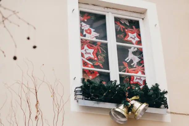 Photo of Stylish christmas decorations, jingle bells, garland lights, fir branches,reindeers  on window in european city street. Festive decor and illumination in city center, winter holidays