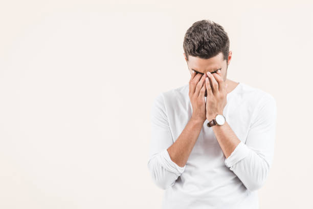 istock upset young man closing eyes with hands isolated on beige 1055214618