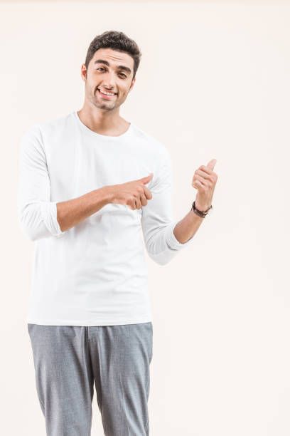 istock handsome young man pointing at copy space and smiling at camera isolated on beige 1055214620