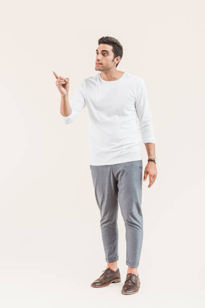 istock handsome young man looking away and pointing with finger isolated on beige 1055214622