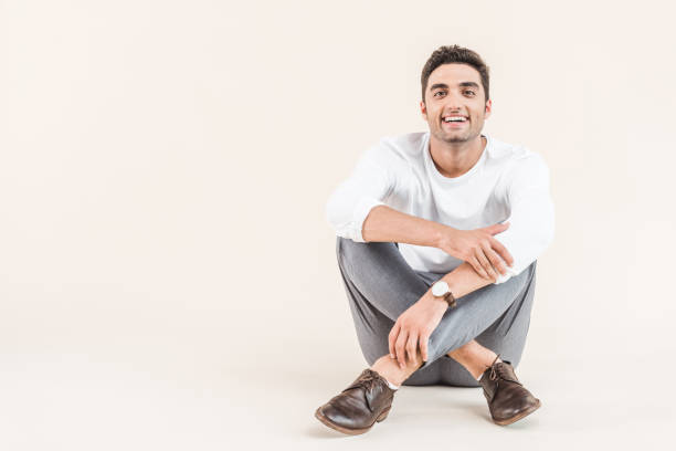 istock cheerful young man sitting and smiling at camera isolated on beige 1055214878