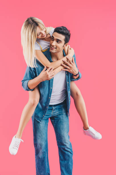 istock handsome young man doing piggyback ride to smiling girlfriend isolated on pink 1055216006
