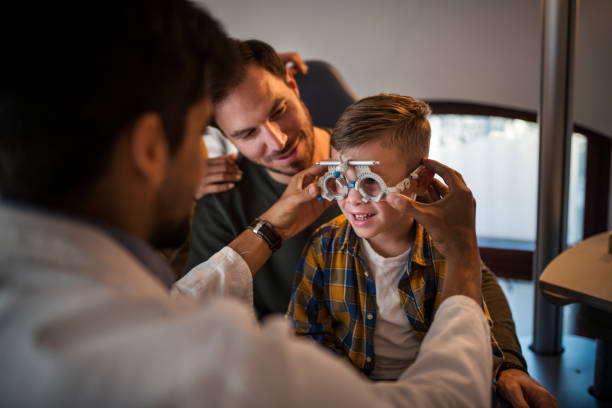 os pais trouxeram o seu filho pequeno para um exame de visão no consultório do oftalmologista. - eye exam senior adult medical equipment men - fotografias e filmes do acervo