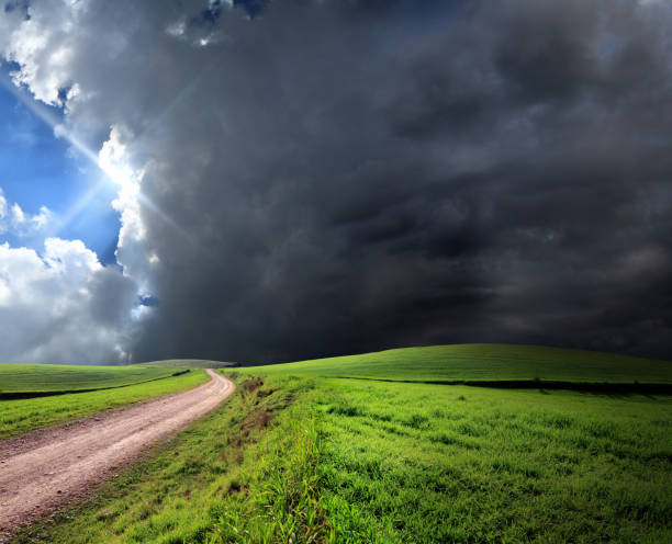 feldweg in grüne landschaft über gewitterhimmel mit sonnenstrahl - incoming storm stock-fotos und bilder