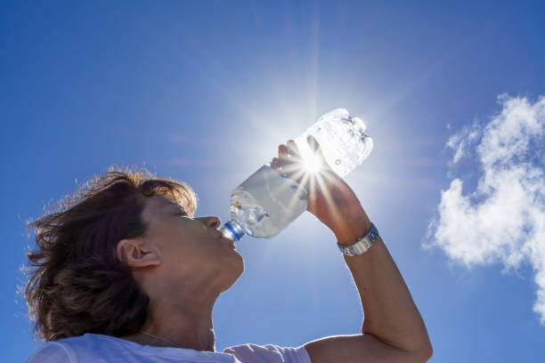 женщина, старшая, питьевая вода в солнечном свете, обратно освещенное изображение с солнечными лучами. - испытывающий жажду стоковые фото и изображения