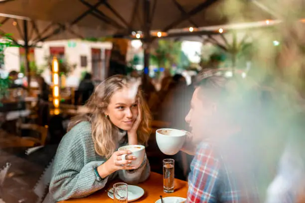 Young caucasian couple enjoying their coffee in a bar. View through the window.