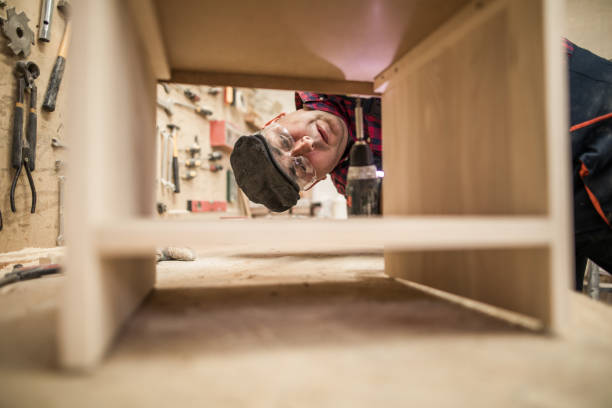 Unrecognized luthier working in his workshop and using glue in a wood board.