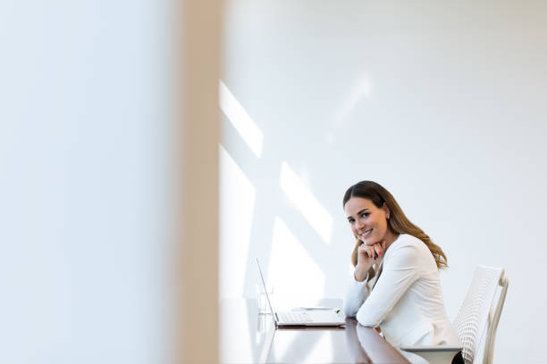 Young latin business woman smiling at the camera while working on her laptop in her office