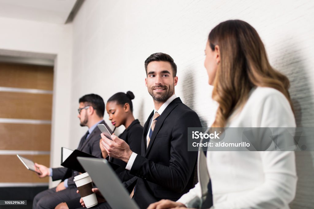 Business team sitting in waiting room and talking A latin business team sitting in a waiting room while talking and reading from devices Adult Stock Photo