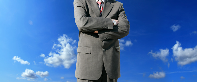 Conceptual close up businessman in suit arms crossed over clear blue sky