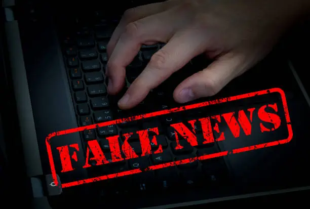 Photo of Fake news with male hand on keyboard in dark room background.