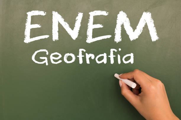 istock Female hand writing with chalk on empty green chalkboard. (translation portuguese: ENEM - National High School Exam Brazil - geography) 1055304224