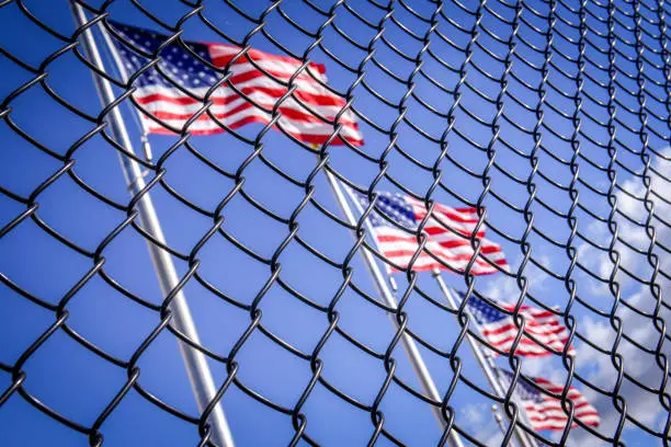 Photo of American flag behind wired fence. Conceptual photo. Border wall to USA