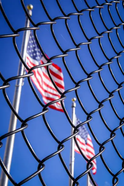 Photo of American flag behind wired fence. Conceptual photo. Border wall to USA