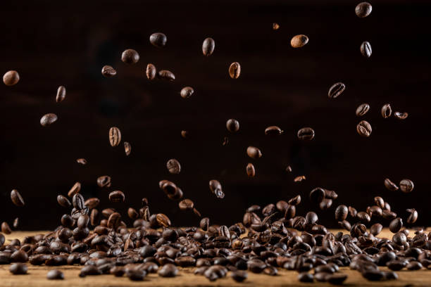 Roasted coffee beans falling down on wooden table stock photo