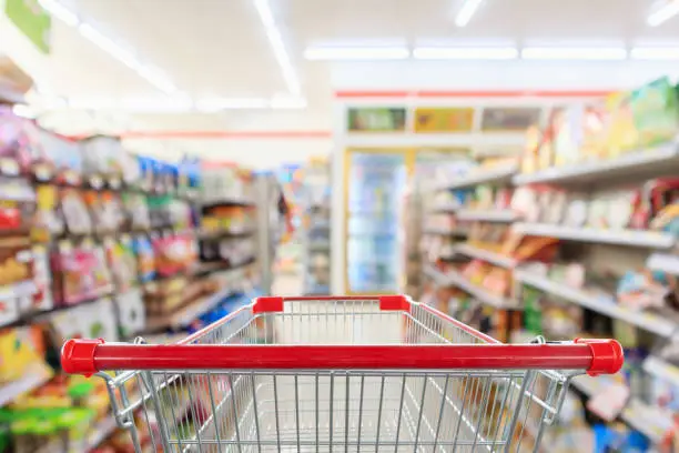 Photo of Shopping cart with Supermarket convenience store aisle shelves interior blur for background