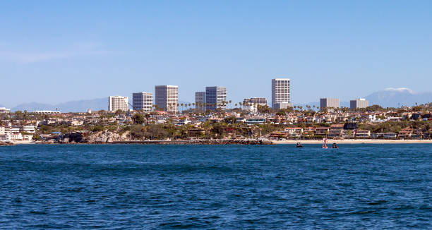 Newport Beach California city skyline with snow capped mountains in the background Newport Beach California city skyline on a sunny day with snow capped San Gabriel mountains ghosting in the background, with entrance to the harbor and Corona Del Mar state beach in the foreground newport beach california stock pictures, royalty-free photos & images