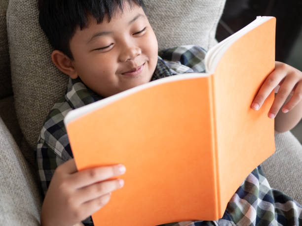 istock Cute asian children reading a book while lying on a sofa in the room. education concept 1055349852