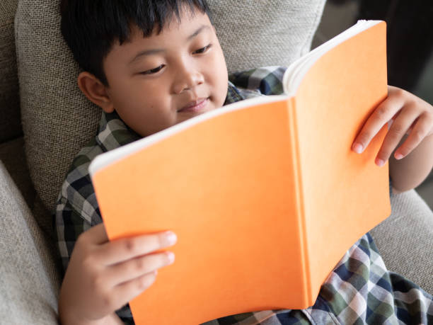 istock Cute asian children reading a book while lying on a sofa in the room. education concept 1055349876