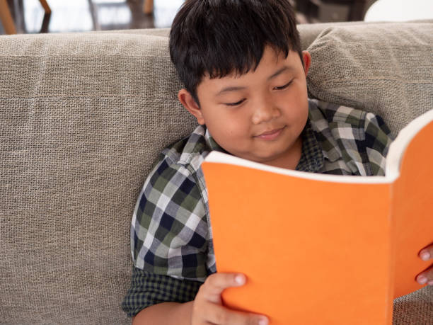 istock Cute asian children reading a book while on a sofa in the room. education concept 1055350058