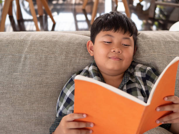 istock Cute asian children reading a book while on a sofa in the room. education concept 1055350118