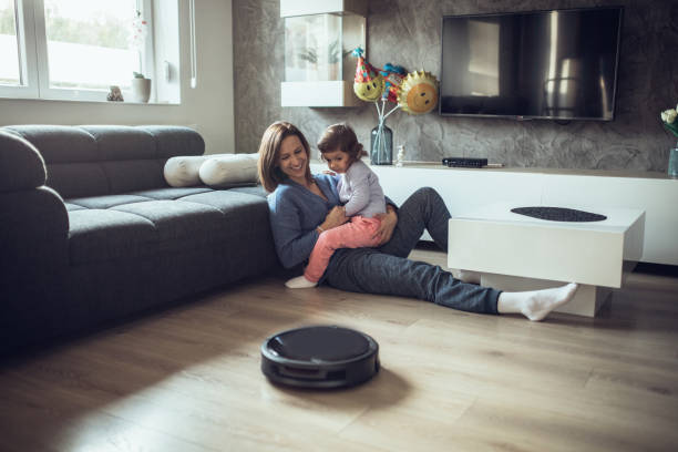 Relaxing while vacuum cleaner works One woman, at home relaxing with her little daughter on the floor, while robot vacuum cleaner is working. smart home family stock pictures, royalty-free photos & images