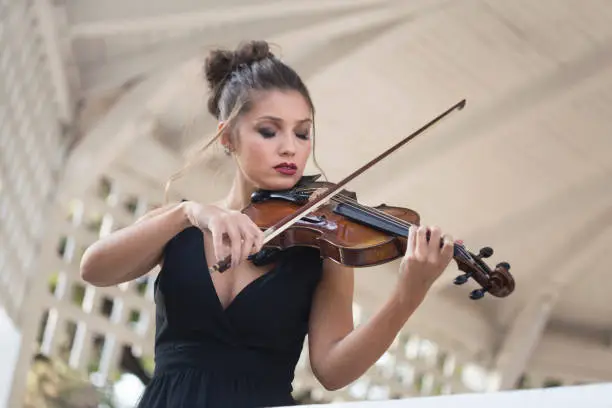 Female violinist playing a violin outdoors in a music pavilion or bandstand. About 25 years old, Caucasian woman.