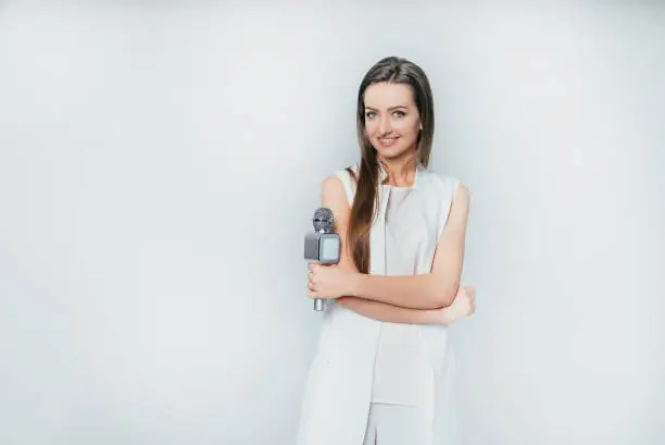 Photo of pretty presenter holds in her hand a microphone on a white background in the studio.