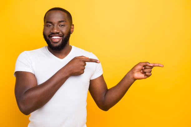 istock Handsome attractive manly cheerful glad satisfied man, pointing with two fingers aside, isolated over bright vivid yellow background 1055427258