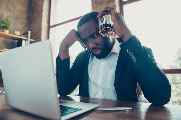 vista a bassa angolazione di elegante elegante squalo d'affari professionista, uomo barbuto mulato in giacca con bicchiere da vino, avere problemi, rivedere il rapporto in laptop sul posto di lavoro, stazione di lavoro - mulato foto e immagini stock