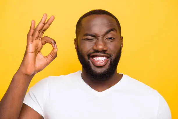 Close-up portrait of handsome glad bearded funky guy showing ok-sign, isolated over bright vivid yellow background