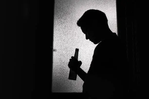 Unrecognizable sad man drinking a beer alone in a dark room.