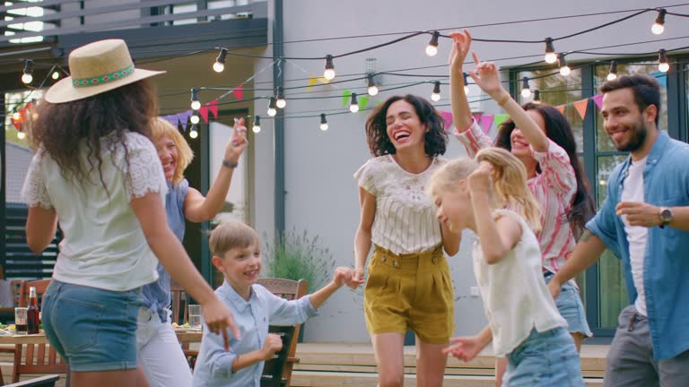 Family and Friends Dancing together at the Garden Party Celebration. Adults and Children Having Fun on a Sunny Summer Day Disco.