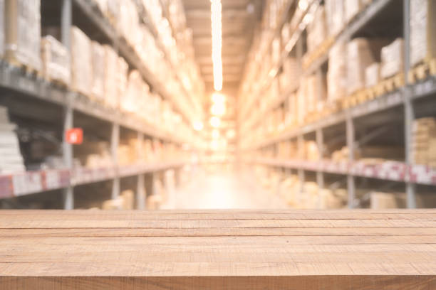 istock Empty wooden table on defocused blurred boxes on rows of shelves in warm light warehouse background. 1055440190