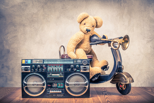 Retro ghetto blaster radio cassette tape recorder and Teddy Bear on old black toy scooter from circa 80s front concrete textured wall background. Listening music concept. Vintage style filtered photo